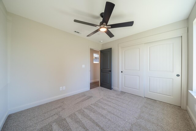 unfurnished bedroom with ceiling fan, light colored carpet, visible vents, baseboards, and a closet