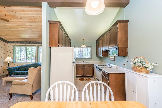 kitchen with lofted ceiling, white appliances, pendant lighting, sink, and light colored carpet