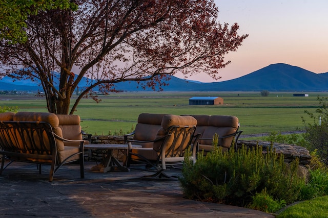 patio terrace at dusk featuring a mountain view and a rural view