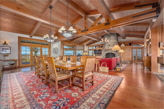 dining room with wood ceiling, a stone fireplace, beam ceiling, a chandelier, and hardwood / wood-style flooring