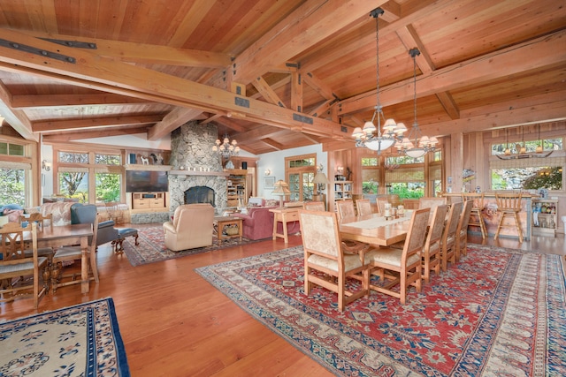 dining area featuring a stone fireplace, wood-type flooring, beamed ceiling, and a chandelier