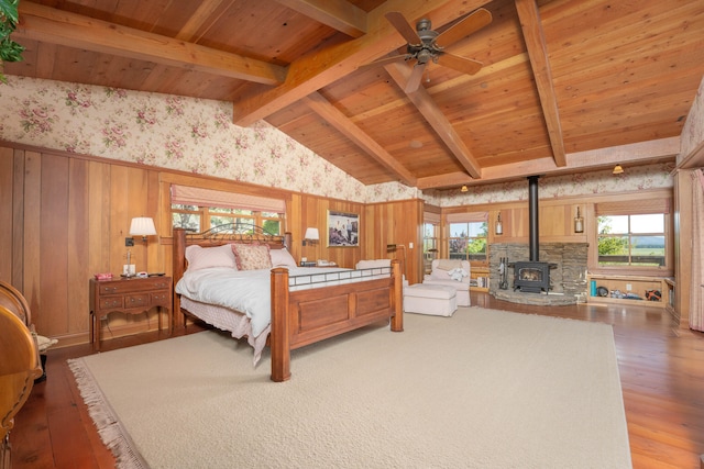 bedroom with a wood stove, multiple windows, light wood-type flooring, and vaulted ceiling with beams