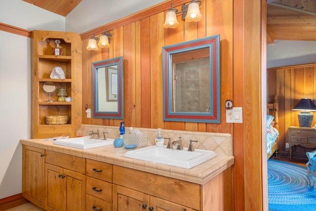 bathroom featuring lofted ceiling, wood walls, tasteful backsplash, and dual bowl vanity