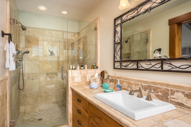 bathroom with a shower with shower door, vanity, and tasteful backsplash