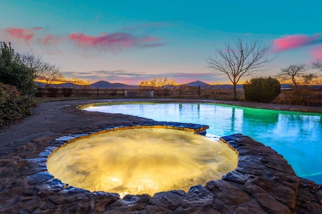 pool at dusk with an in ground hot tub