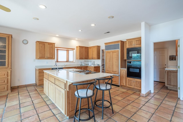 kitchen with light tile patterned flooring, black appliances, a kitchen bar, and a kitchen island with sink