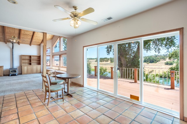 unfurnished dining area featuring vaulted ceiling with beams, a wood stove, wooden ceiling, light carpet, and ceiling fan