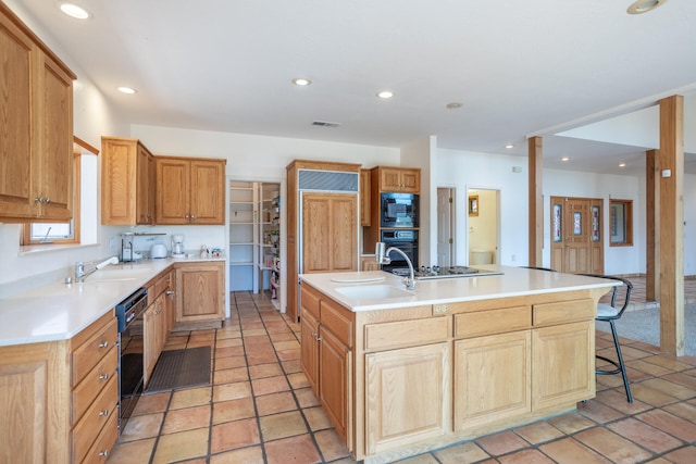 kitchen featuring sink, black appliances, light tile patterned floors, and a center island with sink