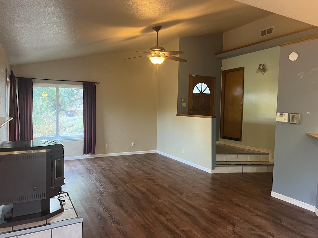 unfurnished living room with lofted ceiling, a textured ceiling, a wood stove, dark hardwood / wood-style flooring, and ceiling fan