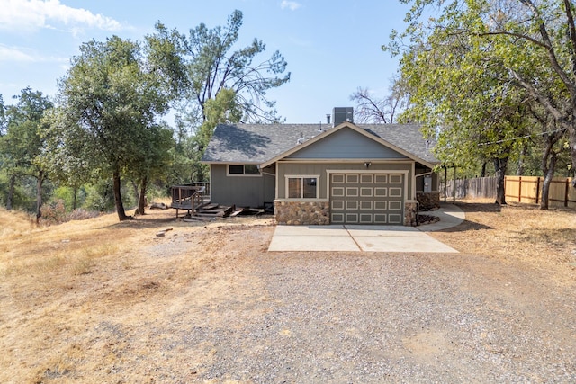 view of front of house featuring concrete driveway, stone siding, an attached garage, fence, and central air condition unit