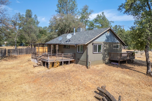 rear view of house with a chimney, roof with shingles, fence, and a deck