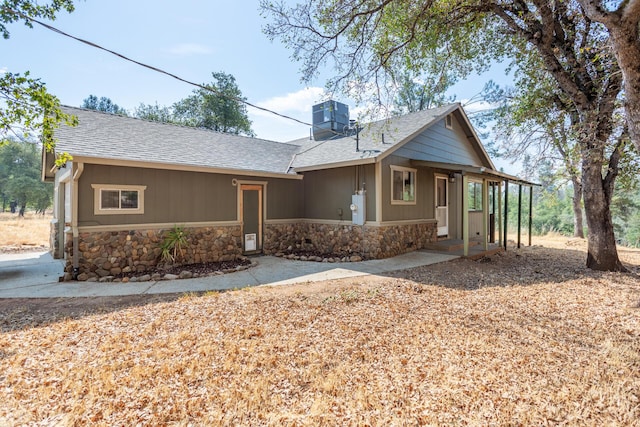 ranch-style house with stone siding, central AC, and roof with shingles