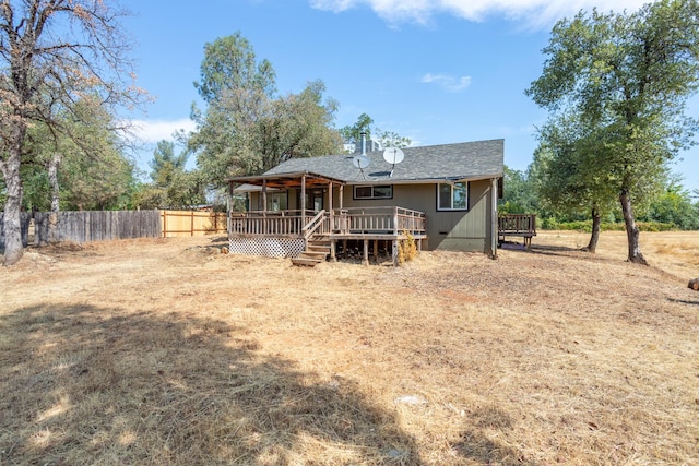 back of house with a shingled roof, a wooden deck, and fence