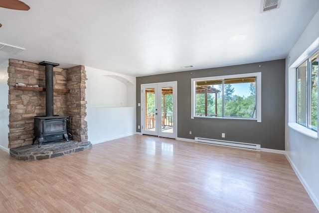 unfurnished living room featuring a wood stove, baseboard heating, wood finished floors, and visible vents