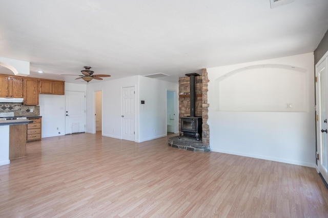 unfurnished living room featuring ceiling fan, visible vents, baseboards, light wood-style floors, and a wood stove