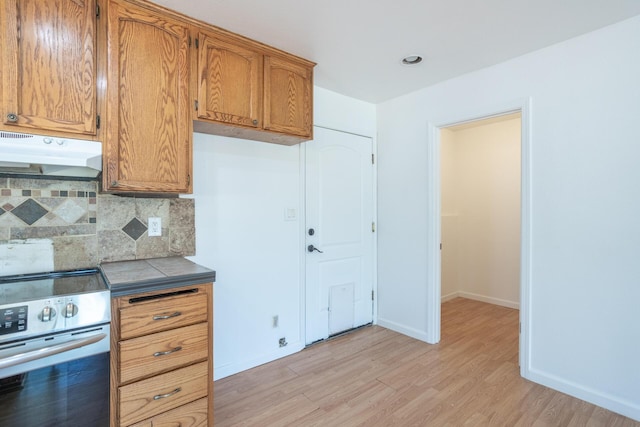 kitchen with tasteful backsplash, electric range, light wood-type flooring, under cabinet range hood, and baseboards