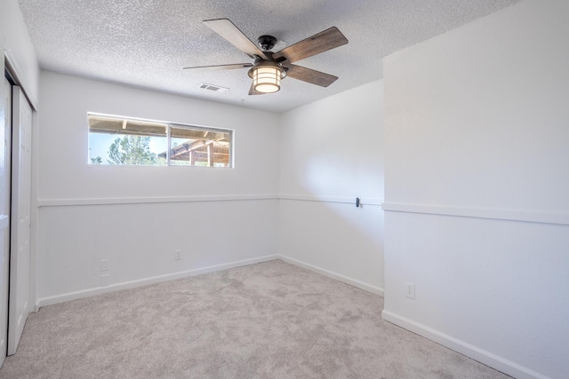 carpeted spare room with baseboards, ceiling fan, visible vents, and a textured ceiling