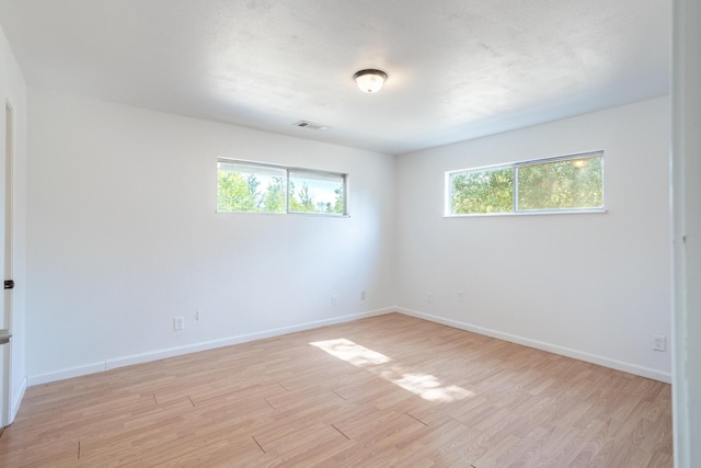 empty room featuring baseboards, visible vents, light wood finished floors, and a textured ceiling