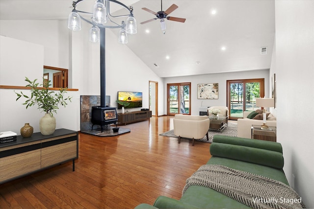 living room with ceiling fan, a wood stove, hardwood / wood-style floors, and high vaulted ceiling