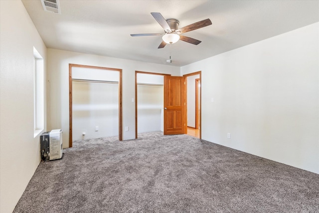 unfurnished bedroom featuring ceiling fan, carpet floors, and two closets