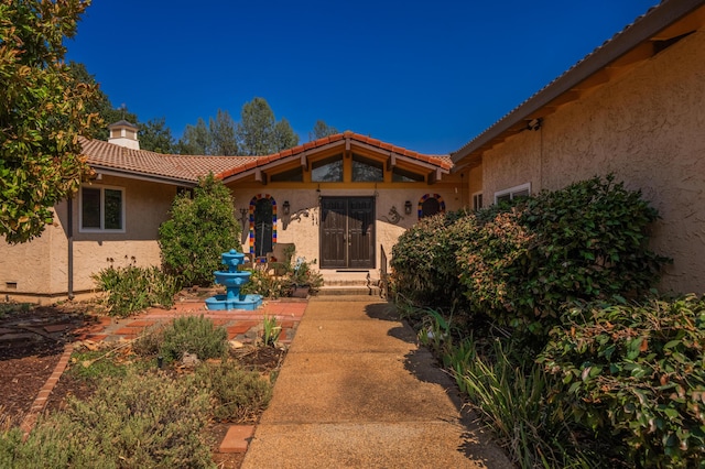 entrance to property with a tile roof, a chimney, and stucco siding