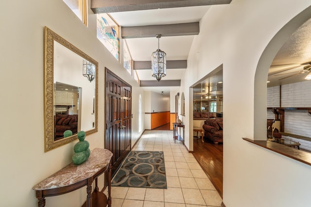 entrance foyer featuring ceiling fan with notable chandelier, plenty of natural light, beamed ceiling, and light tile patterned floors