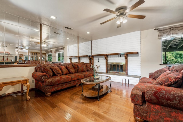 living area featuring a ceiling fan, a fireplace, visible vents, and wood finished floors