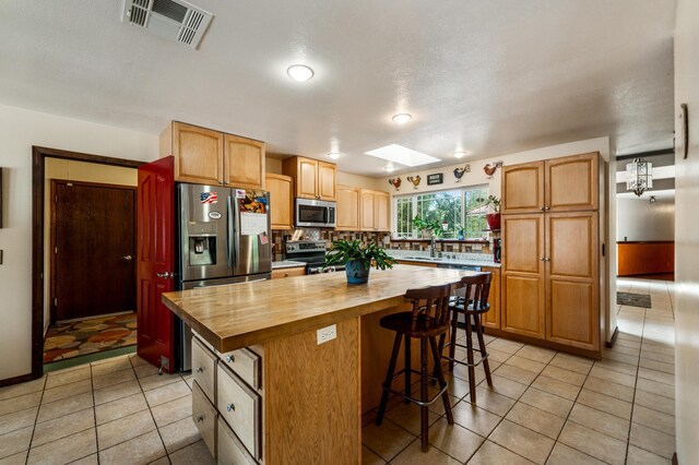 kitchen with light tile patterned flooring, a kitchen island, wooden counters, and stainless steel appliances