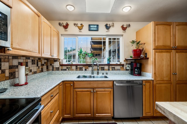 kitchen with light tile patterned floors, appliances with stainless steel finishes, a sink, light stone countertops, and backsplash