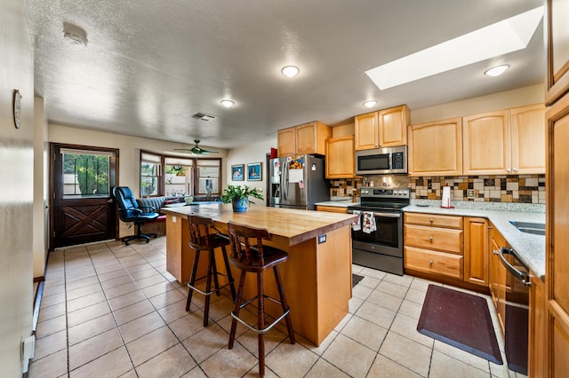 kitchen with appliances with stainless steel finishes, wooden counters, a skylight, a center island, and ceiling fan