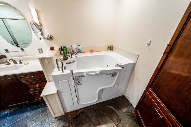 full bath with stone finish floor, vanity, and a bath