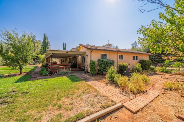 back of house with a chimney, a tiled roof, a deck, a yard, and stucco siding