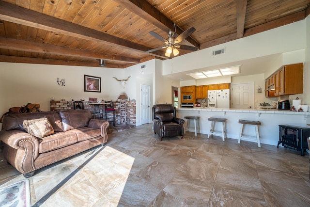 living room with beam ceiling, visible vents, a ceiling fan, a wood stove, and wooden ceiling