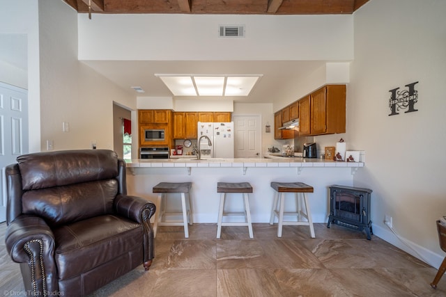 kitchen featuring tile countertops, oven, a breakfast bar, brown cabinets, and stainless steel microwave