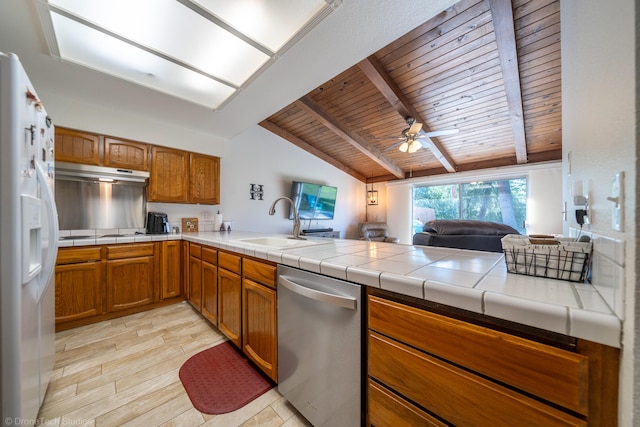 kitchen featuring white refrigerator with ice dispenser, tile countertops, stainless steel dishwasher, open floor plan, and a peninsula