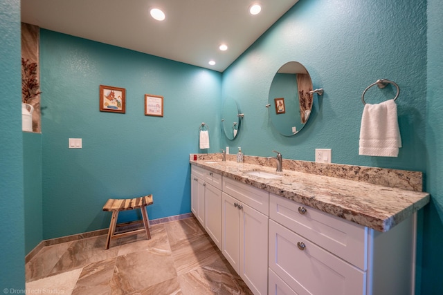 bathroom featuring double vanity, baseboards, a sink, and recessed lighting