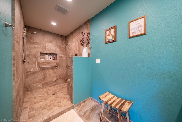 full bath featuring visible vents, a textured wall, baseboards, and tiled shower