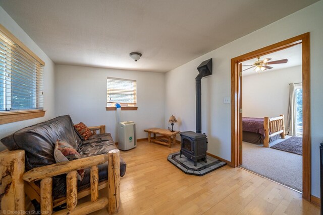 living room featuring a wood stove, light wood-type flooring, and ceiling fan