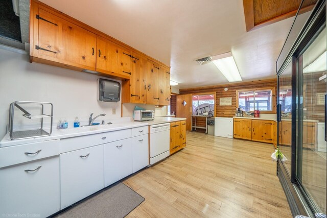 kitchen featuring wood walls, light wood-type flooring, white dishwasher, and sink