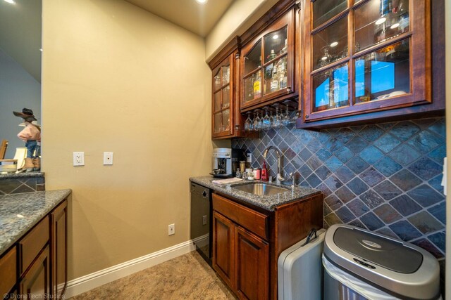 bar featuring dark stone countertops, dishwasher, backsplash, light tile patterned floors, and sink