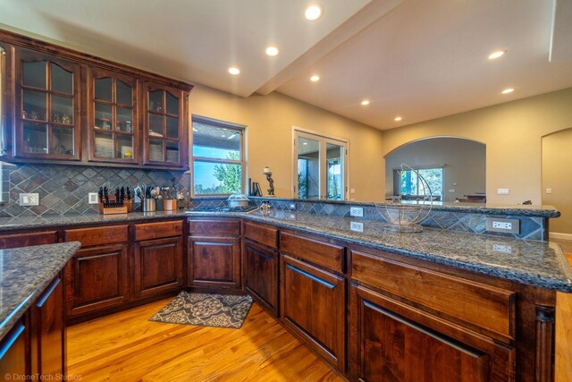 kitchen with kitchen peninsula, dark stone countertops, tasteful backsplash, and light hardwood / wood-style floors