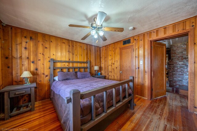 bedroom featuring a textured ceiling, ceiling fan, wood walls, hardwood / wood-style floors, and brick wall