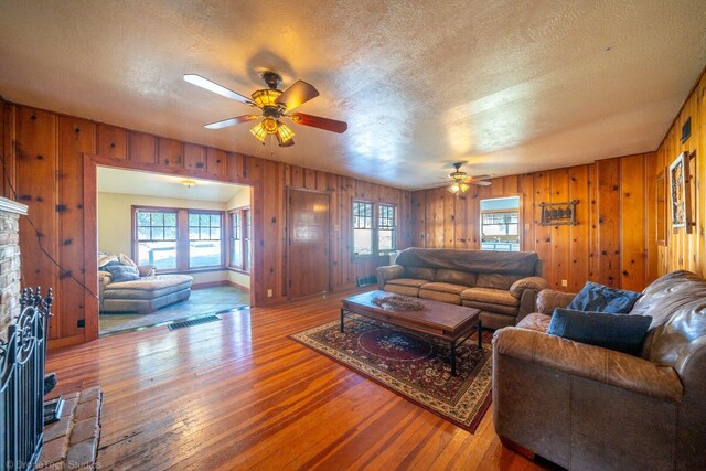 living room featuring hardwood / wood-style floors, wooden walls, a wealth of natural light, and ceiling fan