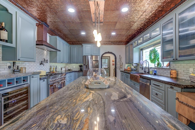 kitchen with pendant lighting, appliances with stainless steel finishes, dark stone countertops, wine cooler, and custom range hood