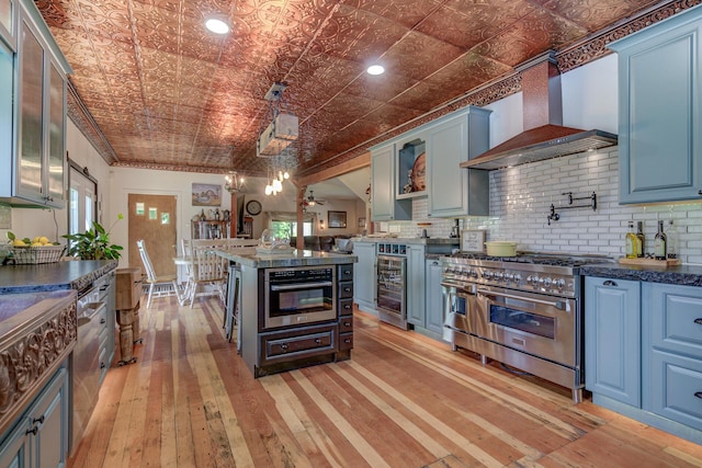 kitchen with wall chimney range hood, pendant lighting, backsplash, stainless steel appliances, and beverage cooler