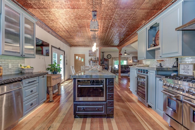 kitchen with light hardwood / wood-style floors, appliances with stainless steel finishes, decorative backsplash, decorative light fixtures, and beverage cooler