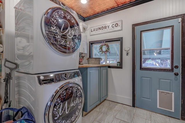 clothes washing area with crown molding, cabinets, and stacked washer and dryer