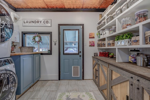 laundry area with stacked washer / drying machine, ornamental molding, and cabinets