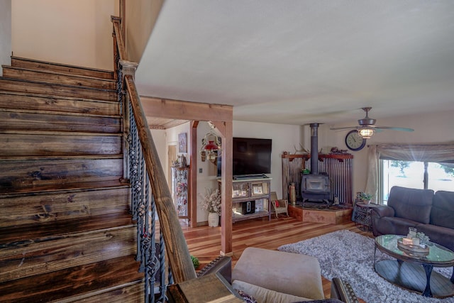 living room with ceiling fan, a wood stove, and wood-type flooring