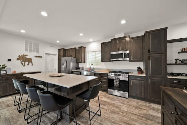 kitchen featuring appliances with stainless steel finishes, light hardwood / wood-style floors, dark brown cabinetry, a kitchen breakfast bar, and a center island